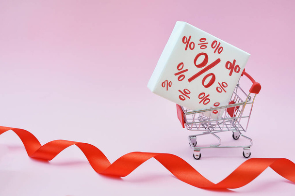 Image of empty shopping trolley or cart with box of discount percent sale black Friday products on pink background. Concept of sell or buy with place for your text - Photo, Image