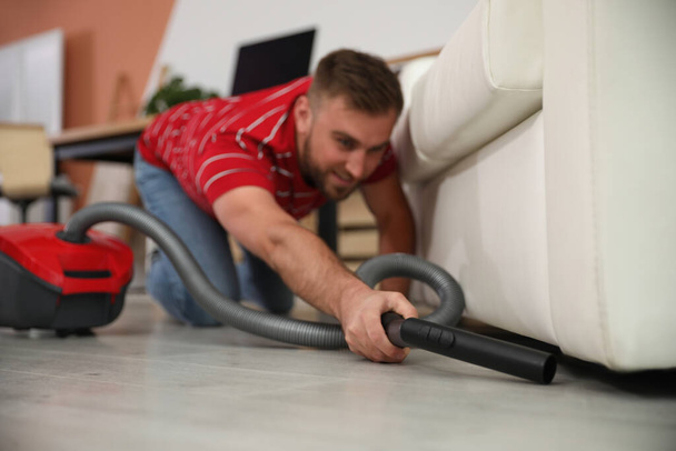 Young man using vacuum cleaner in living room - Foto, afbeelding
