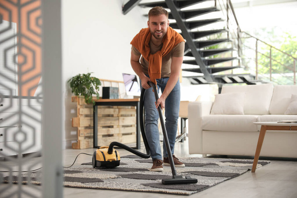 Young man using vacuum cleaner in living room - Foto, afbeelding