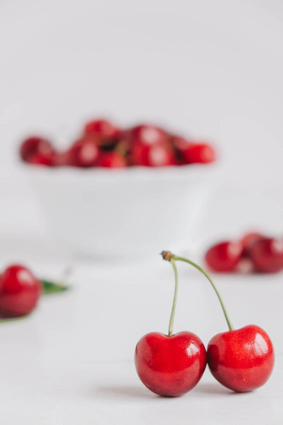 Čerstvé šťavnaté červené třešně v bílém talíři na bílém dřevěném pozadí. Kopírovat, prázdné místo pro text. - Fotografie, Obrázek