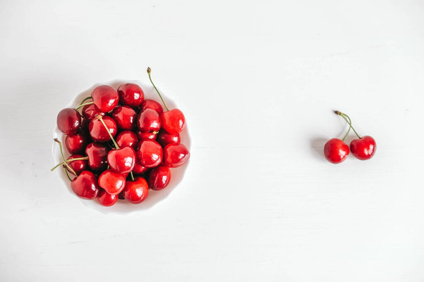 Fresh juicy red cherries in a white plate on the white wooden background. Top view. Copy, empty space for text. - Photo, Image