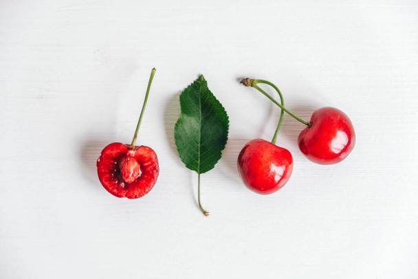 Fresh ripe cherries with green leav on the white wooden background. Top view. Copy, empty space for text. - Fotó, kép