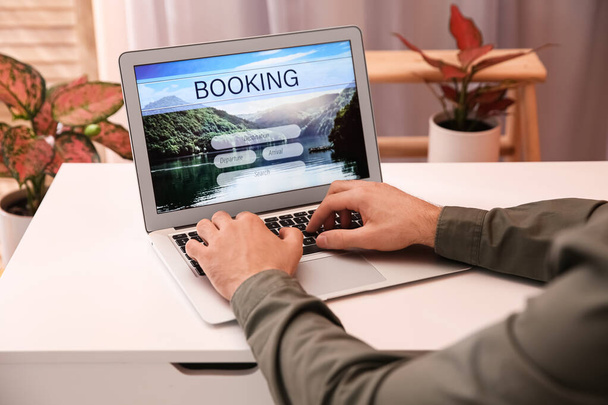 Man with laptop booking tickets online at white table, closeup. Travel agency concept - Φωτογραφία, εικόνα