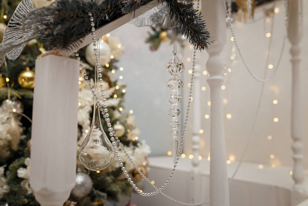Soft focused shot of beads and artificial icicles on fir tree and golden shiny Christmas lights bokeh background. Festive atmosphere, holiday spirit, New Year celebration concept. - Photo, Image