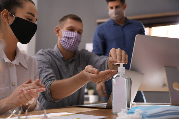 Coworkers with protective masks using hand sanitizer in office. Business meeting during COVID-19 pandemic - Foto, Imagem