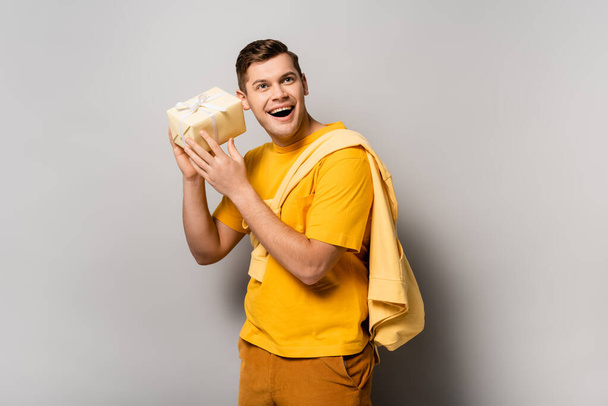 Excited man holding gift box on grey background - Foto, Imagem