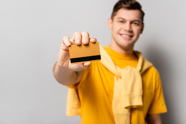 Credit card in hand of smiling man blurred on grey background - Photo, image