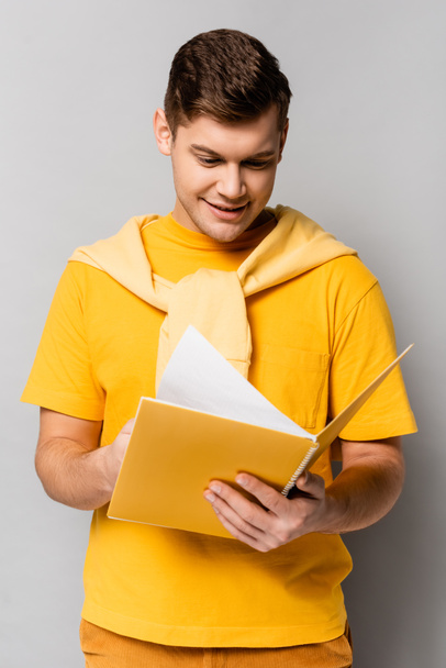 Pozytywny student patrzący na notatnik na szarym tle - Zdjęcie, obraz
