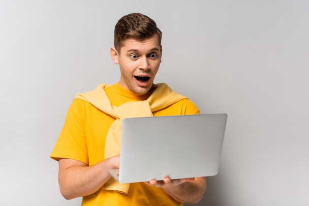 Amazed man with open mouth using laptop on grey background - Photo, Image