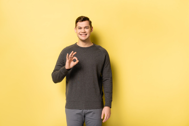 Homem alegre em roupas cinza mostrando sinal ok no fundo amarelo - Foto, Imagem