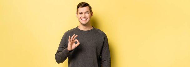 Smiling man showing ok sign on yellow background, banner  - Photo, Image