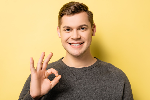 Young man showing okay gesture and looking at camera on yellow background - Foto, afbeelding