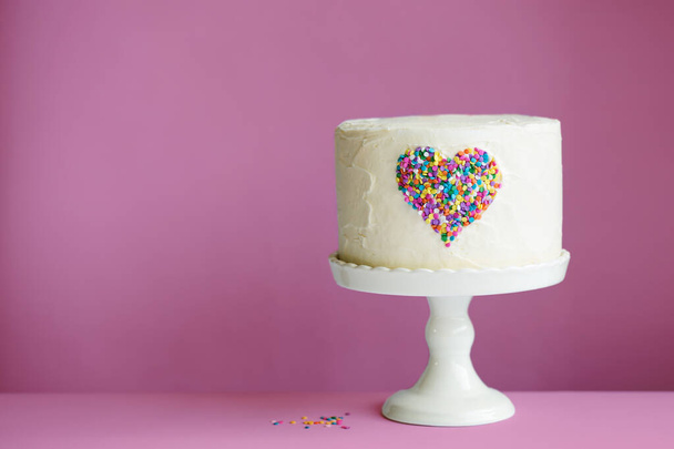 White Valentines cake with colorful heart made of sprinkles on a pink background - Photo, Image