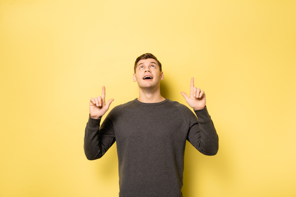 Man pointing with fingers up on yellow background - Foto, afbeelding