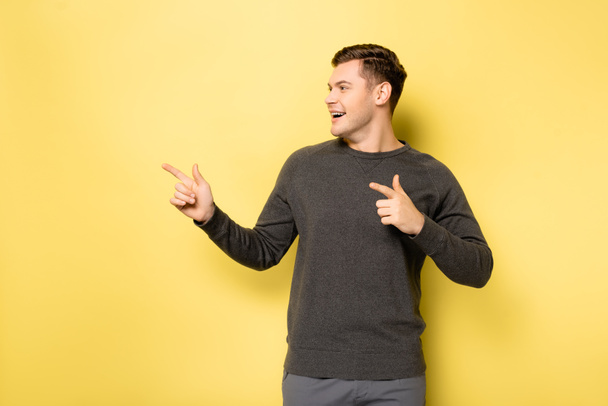 Smiling man pointing with fingers on yellow background - Fotografie, Obrázek