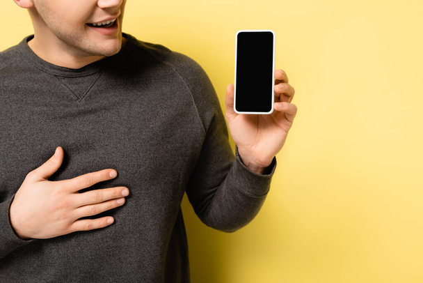 Gewassen weergave van positieve man met smartphone met blanco scherm op gele achtergrond - Foto, afbeelding
