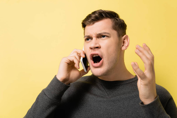 Embarrassed man talking on smartphone on yellow background - Photo, Image