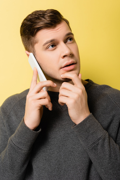 Dreamy man talking on mobile phone on yellow background - Фото, изображение