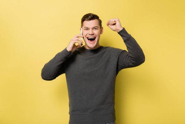 Excited man talking on smartphone and showing yes gesture on yellow background - Fotografie, Obrázek