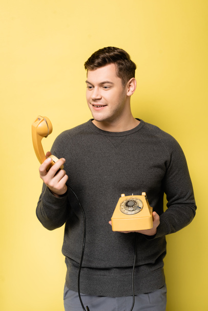 Young man smiling while looking at telephone handset on yellow background - Fotó, kép