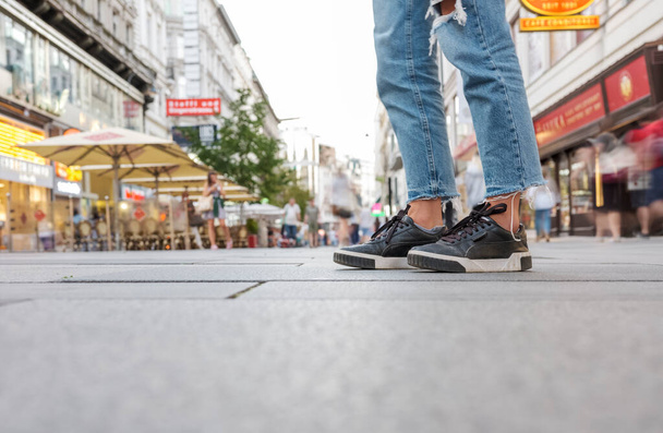 Close up photo of sneakers and blue jeans on a background of a crowded street in the center of Vienna - 写真・画像