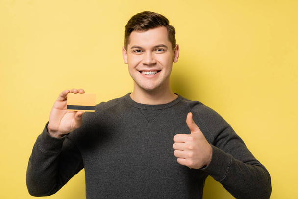 Hymyilevä mies näyttää ja luottokortti keltaisella taustalla - Valokuva, kuva