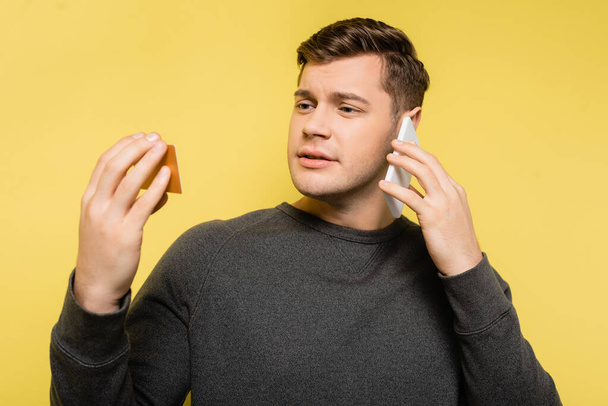 Man talking on telephone and looking at credit card on yellow background - Zdjęcie, obraz