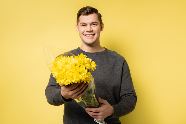 Cheerful man holding flowers on yellow background - Foto, Imagem