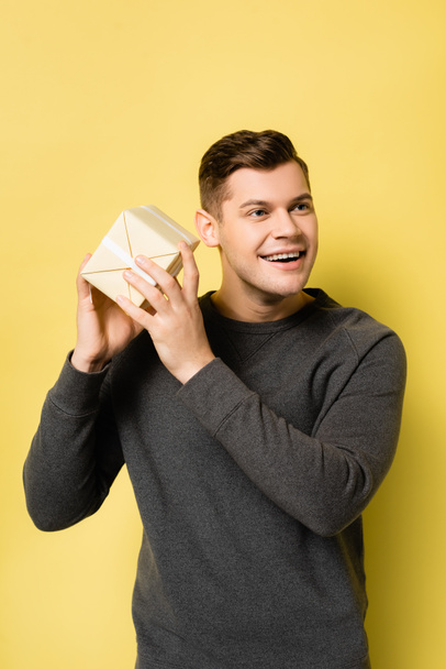 Cheerful man in grey pullover holding present on yellow background - Фото, зображення