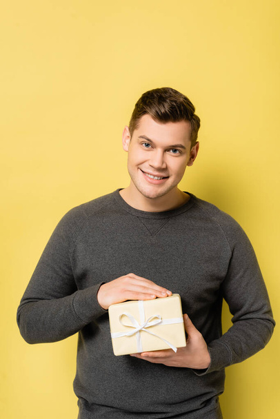 Happy man with present looking at camera on yellow background - Foto, afbeelding