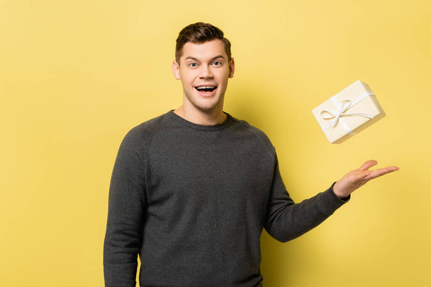 Smiling man throwing gift box on yellow background - Foto, Imagem
