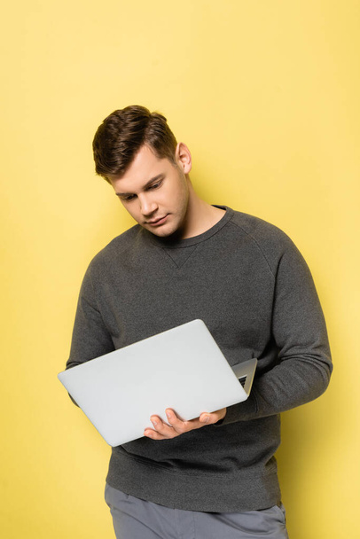 Young man using laptop on yellow background - Fotoğraf, Görsel