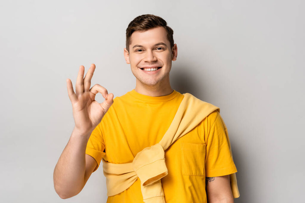 Smiling man in yellow clothes showing ok gesture on grey background - 写真・画像