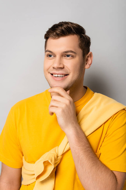 Young happy man in yellow clothes looking away on grey background - Фото, изображение