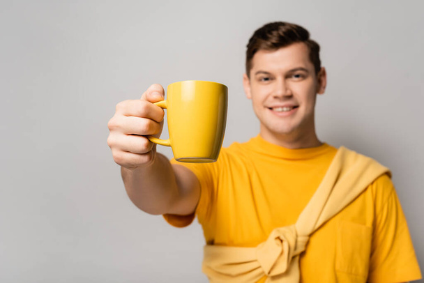 Yellow cup in hand of smiling man blurred on grey background - Foto, afbeelding
