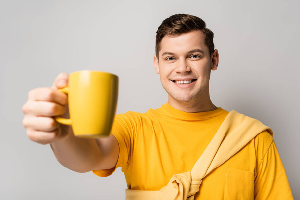 Positive man holding cup on blurred foreground on grey background - Фото, зображення