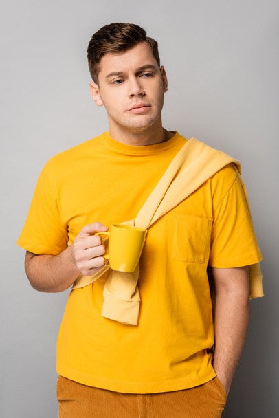 Sad man with yellow cup looking away on grey background - Foto, afbeelding