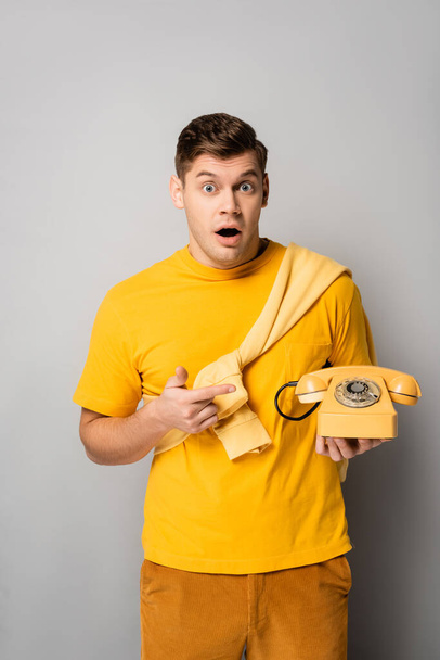 Возбужденный мужчина, указывающий пальцем на винтажный телефон на сером фоне - Фото, изображение