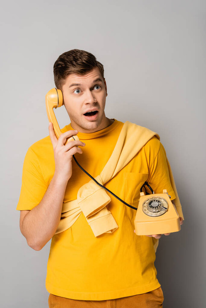 Verbazingwekkende man kijkt omhoog terwijl praten over de telefoon op grijze achtergrond - Foto, afbeelding