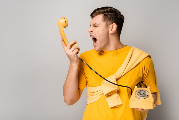 Wütender Mann schreit am Telefonhörer vor grauem Hintergrund - Foto, Bild