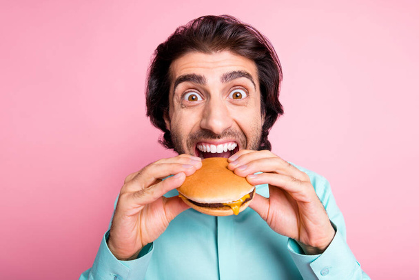 Photo portrait of hungry man taking massive bite of cheeseburger isolated on pastel pink colored background - Photo, image