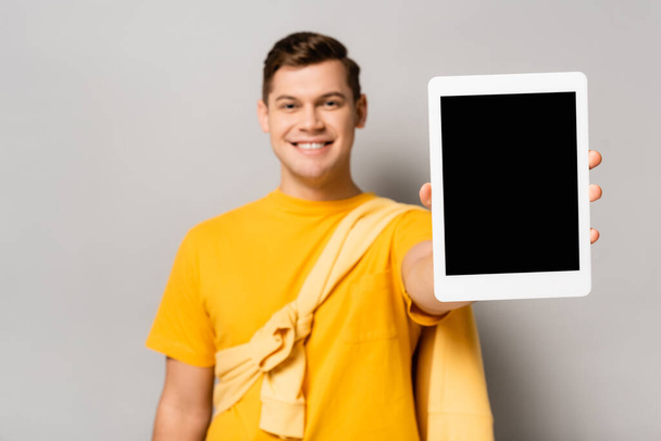Digitales Tablet mit leerem Bildschirm in der Hand eines lächelnden Mannes verschwommen auf grauem Hintergrund - Foto, Bild