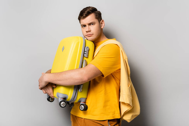 Upset traveler hugging suitcase on grey background - Foto, imagen