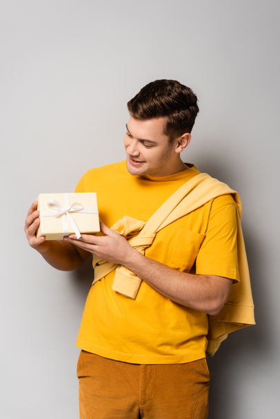 Brunette man in casual clothes looking at gift on grey background - Foto, Bild