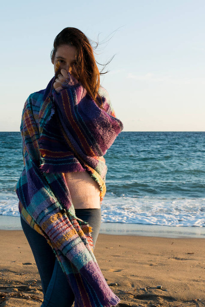 Женщина, завернутая в одеяло, смотрит в камеру на пляже - Фото, изображение