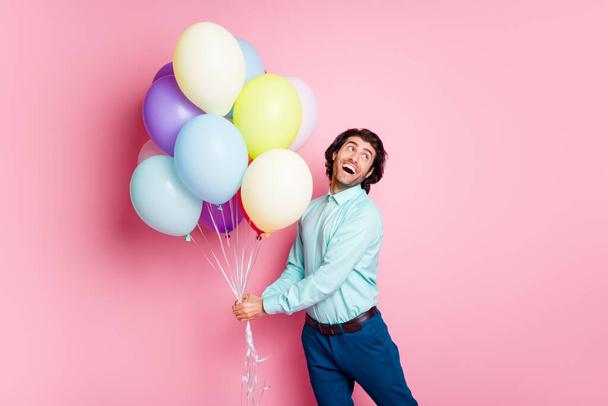 Photo portrait of excited guy holding air ballons in two hands looking to side isolated on pastel pink colored background - Fotoğraf, Görsel