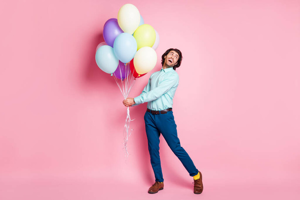 Full length photo portrait of excited man holding air balloons in two hands isolated on pastel pink colored background - Foto, afbeelding