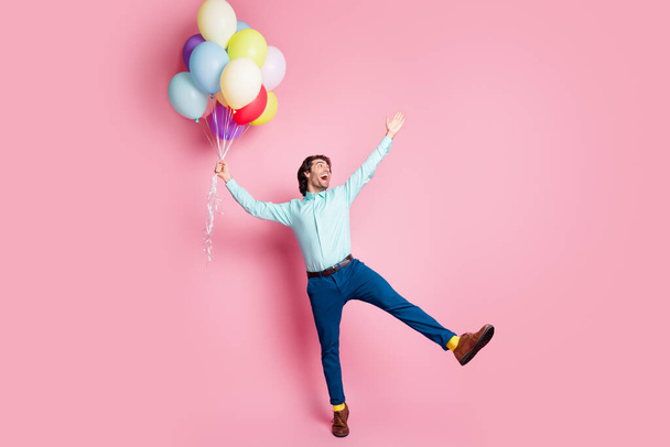 Photo portrait full body view of man spreading legs arms like star standing on one leg holding helium balloons isolated on pastel pink colored background - Foto, imagen