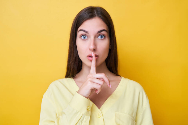 Portrait of brunette girl holding finger on lips, asking to be quiet and keep secret, shhh gesture isolated on yellow studio background - Φωτογραφία, εικόνα