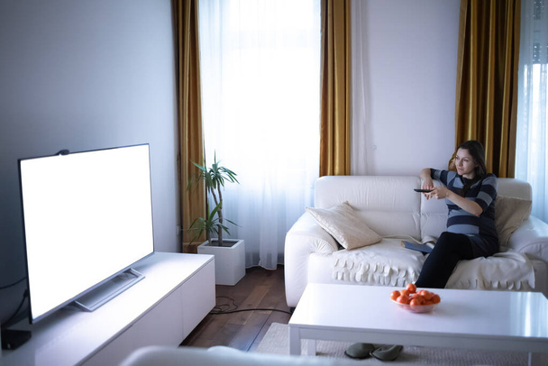 Όμορφη έγκυος γυναίκα βλέποντας τηλεόραση στο μοντέρνο διαμέρισμά της - Φωτογραφία, εικόνα